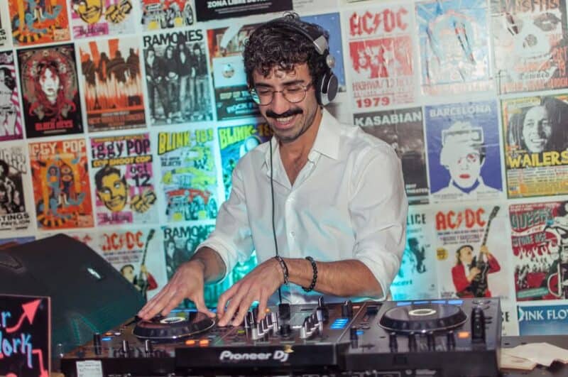 DJ playing music at St Christopher’s Barcelona hostel, with vibrant music posters on the wall behind.