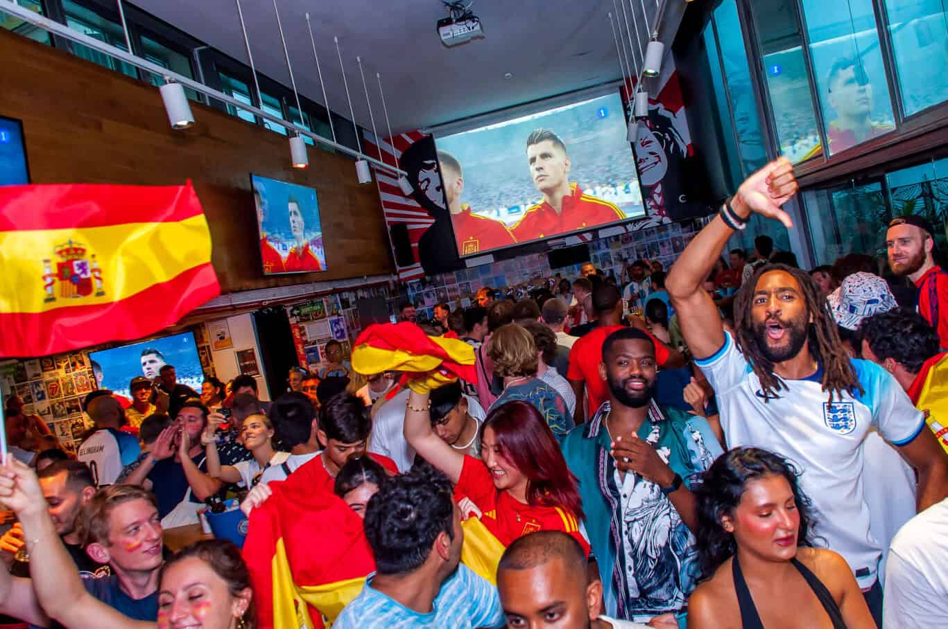Lively crowd celebrating with Spanish flags at St Christopher’s Barcelona hostel bar.
