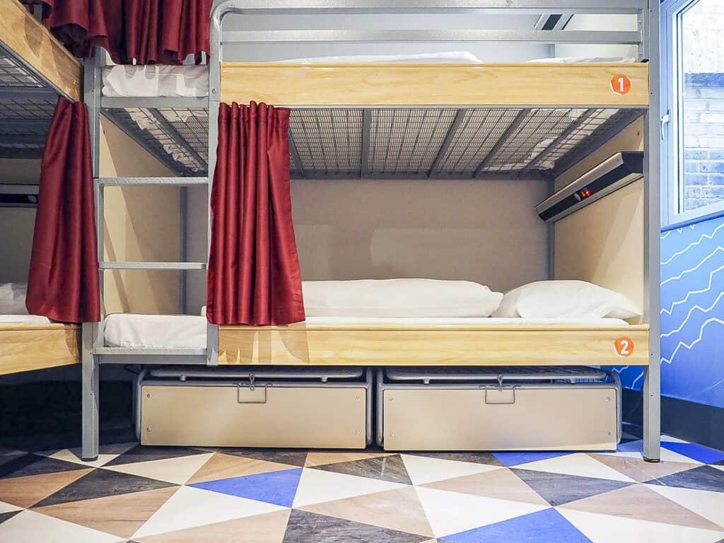 Bunk bed with privacy curtains in a contemporary hostel dormitory setting.