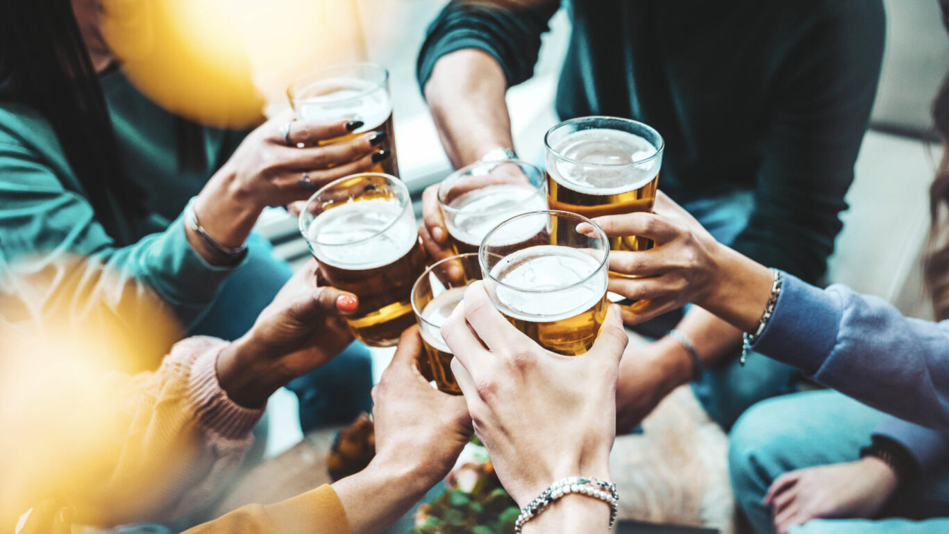 Group of people drinking beer at brewery pub restaurant – Happy friends enjoying happy hour sitting at bar table – Closeup image of brew glasses – Food and beverage lifestyle concept