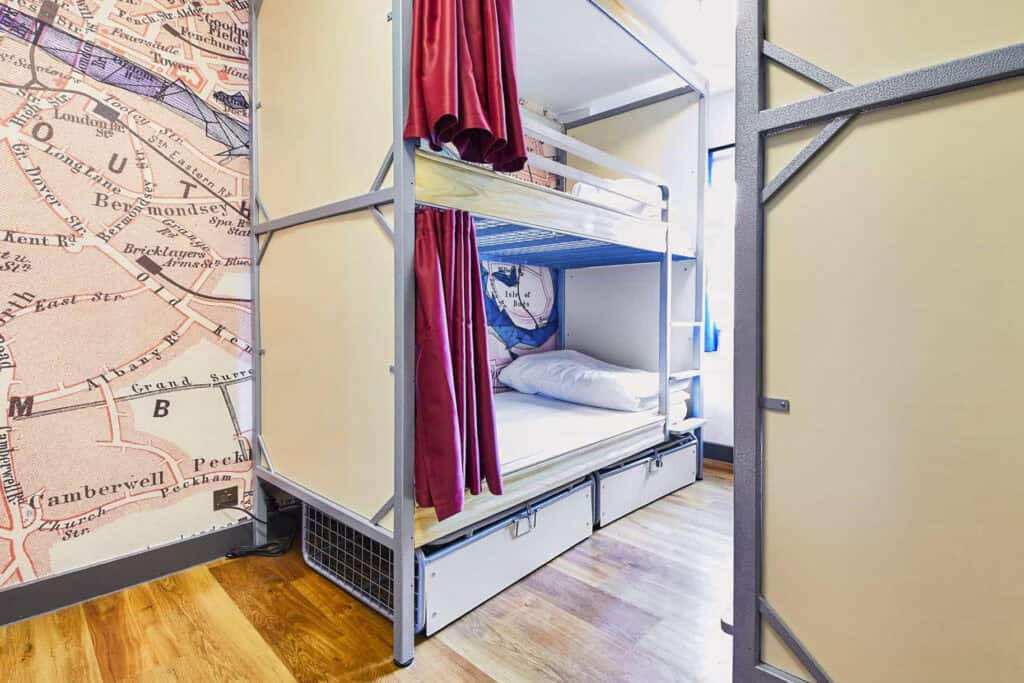 Bunk beds in a hostel room near London Bridge with colourful curtains and map wall decor.