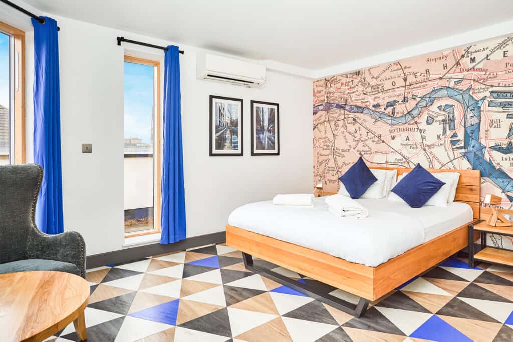 Bright hotel room with a large bed, colourful wall art, and vibrant blue curtains.
