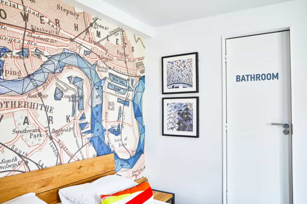 Interior view of a hostel room at St Christopher’s London Bridge with artwork and a bathroom door.