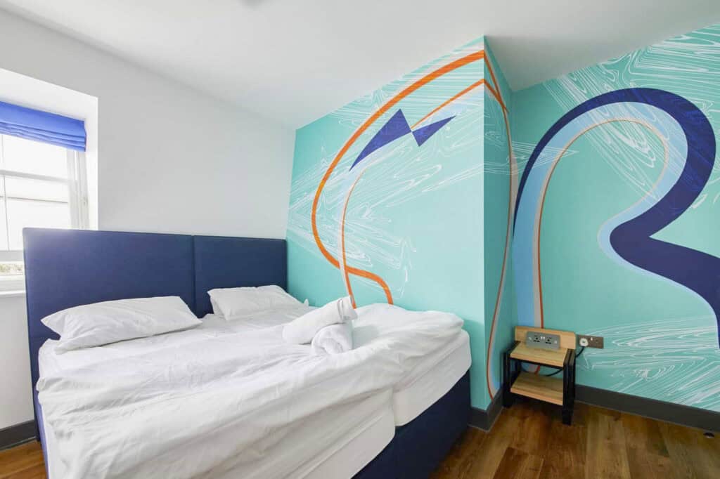 Bright hostel room featuring a vibrant mural and a cosy double bed.