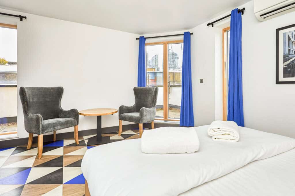 Bright hostel room with large windows and blue curtains.