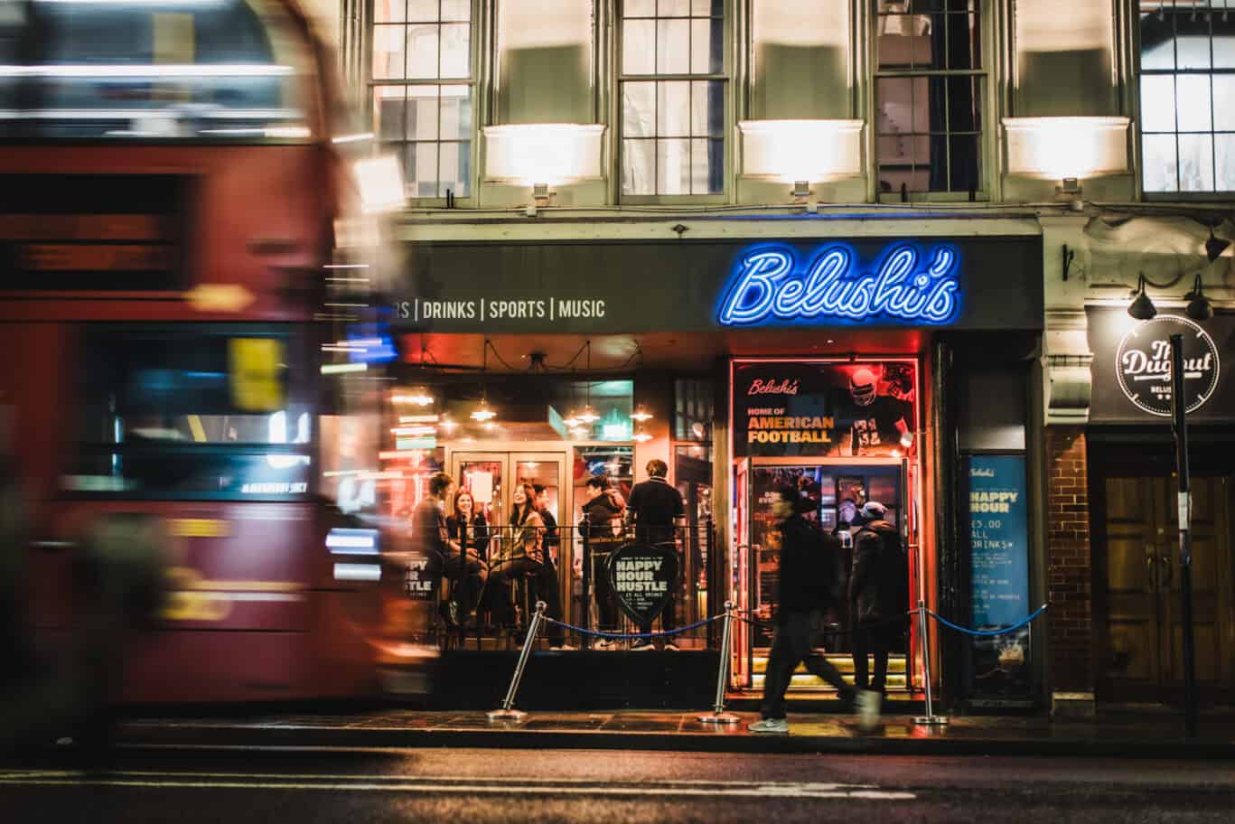 Night scene at Belushi's bar near London Bridge with people and a moving bus.