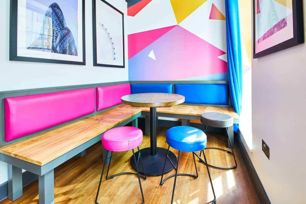 Bright hostel lounge with colourful pink, blue, and grey seating and wall art.