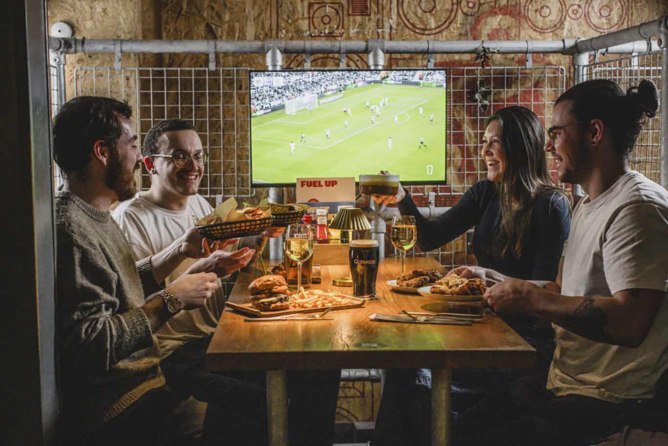 Group of friends enjoying drinks and food while watching a football match at London Bridge Hostel.