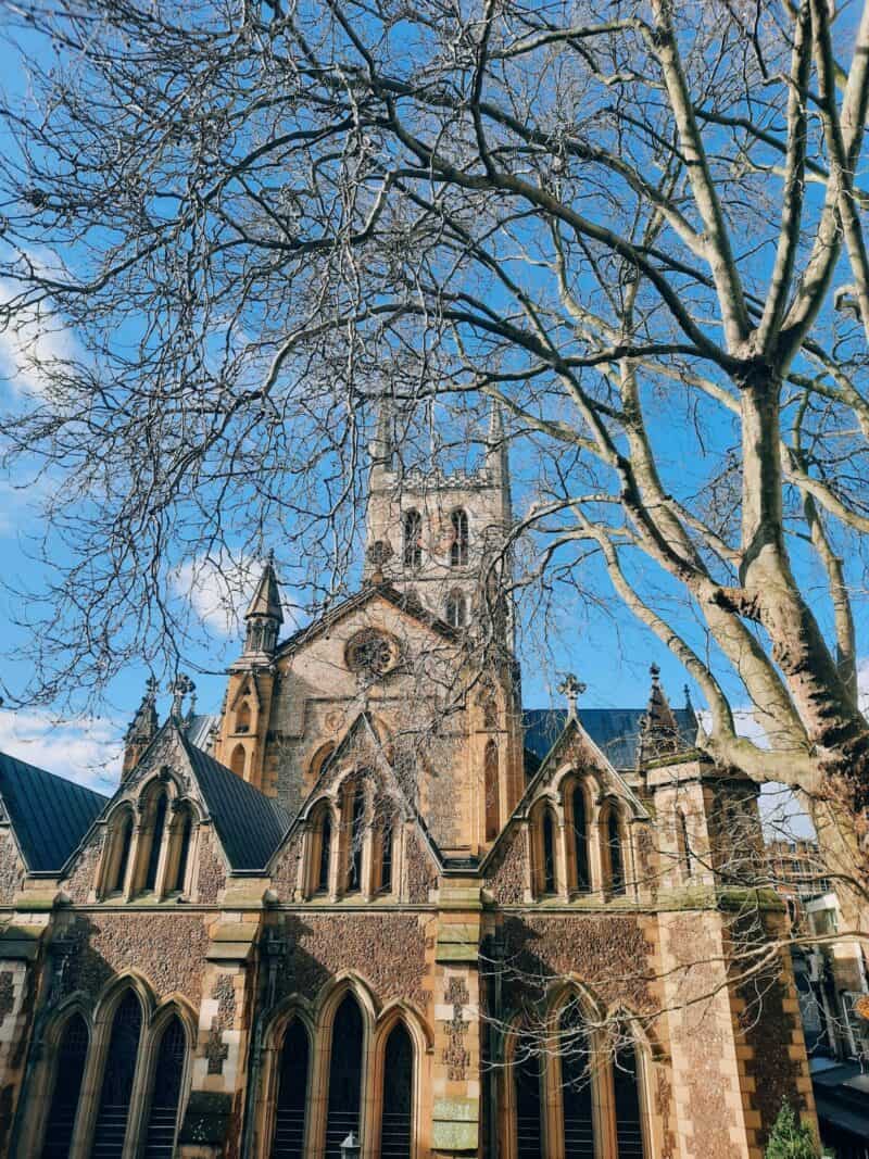 View of historic London Bridge and St Christopher's Inns in London with leafless trees and blue sky.