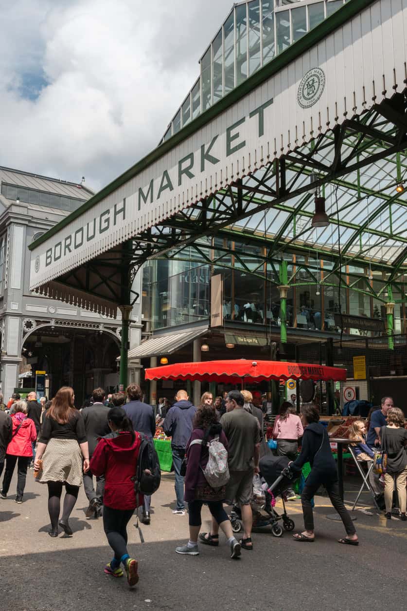 Bustling scene at Borough Market entrance in London with shoppers and food stalls.