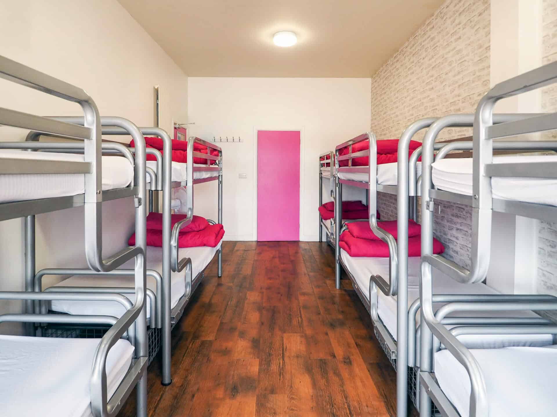 Dormitory room with metal bunk beds and pink bedding at St Christopher’s Newquay hostel.