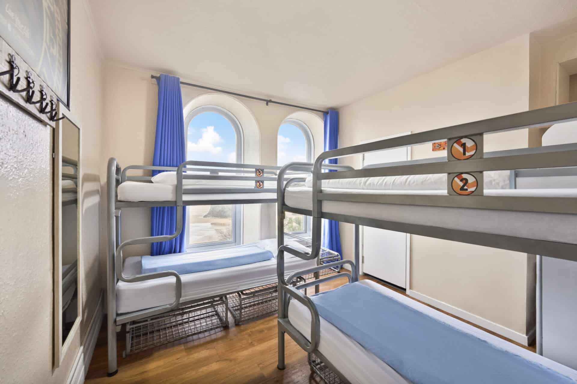 Bunk beds in a bright hostel dormitory at St Christopher’s Newquay, with large windows and ocean vie.