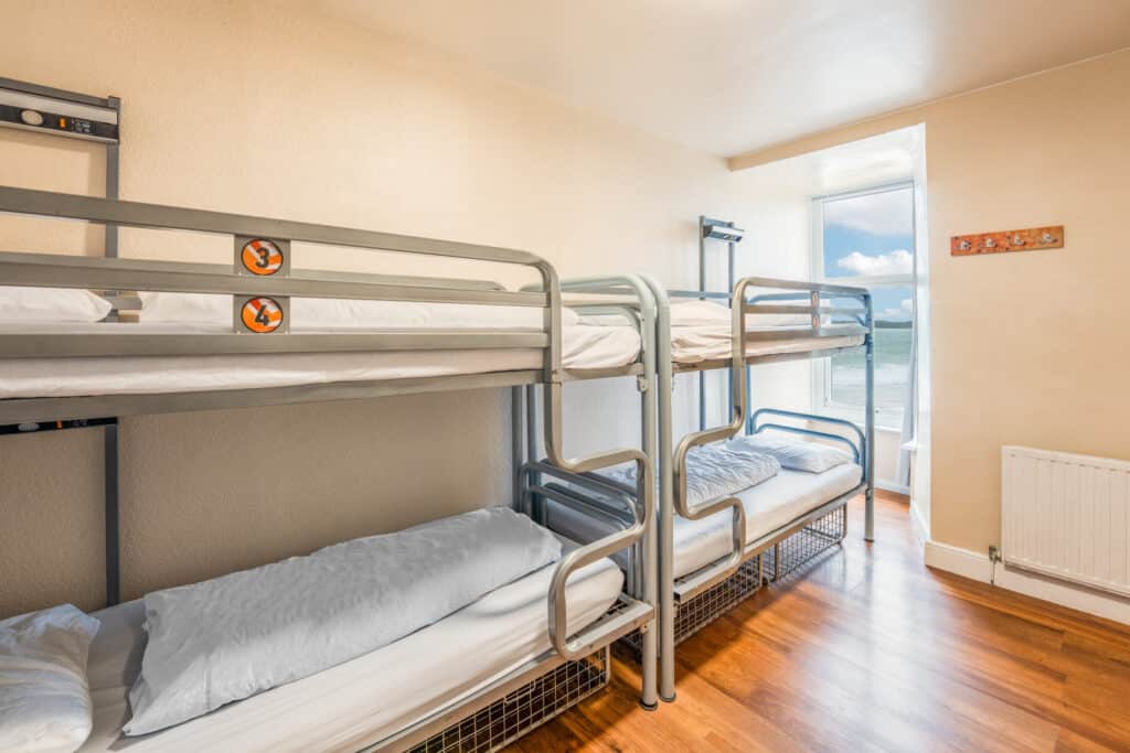 Dormitory room at St Christopher’s Newquay hostel with metal bunk beds and ocean view.