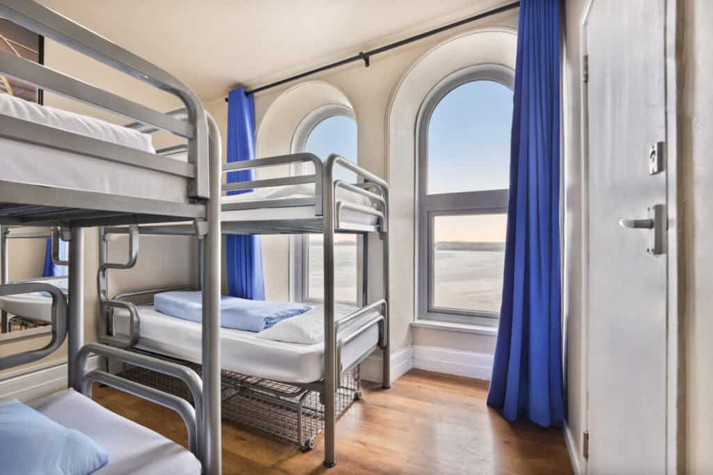 Hostel dorm room with bunk beds, large windows, and sea view at St Christopher’s Newquay.