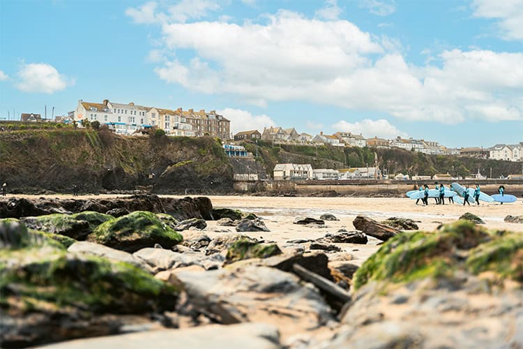 View of Newquay beach with surfers and colourful houses in the background.