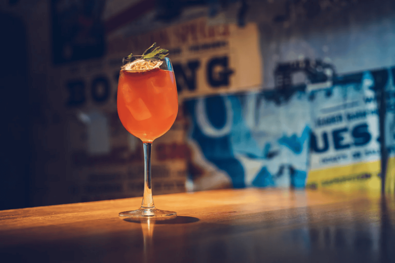 An inviting orange cocktail garnished with herbs on a wooden bar counter at St Christopher’s Edinbur.