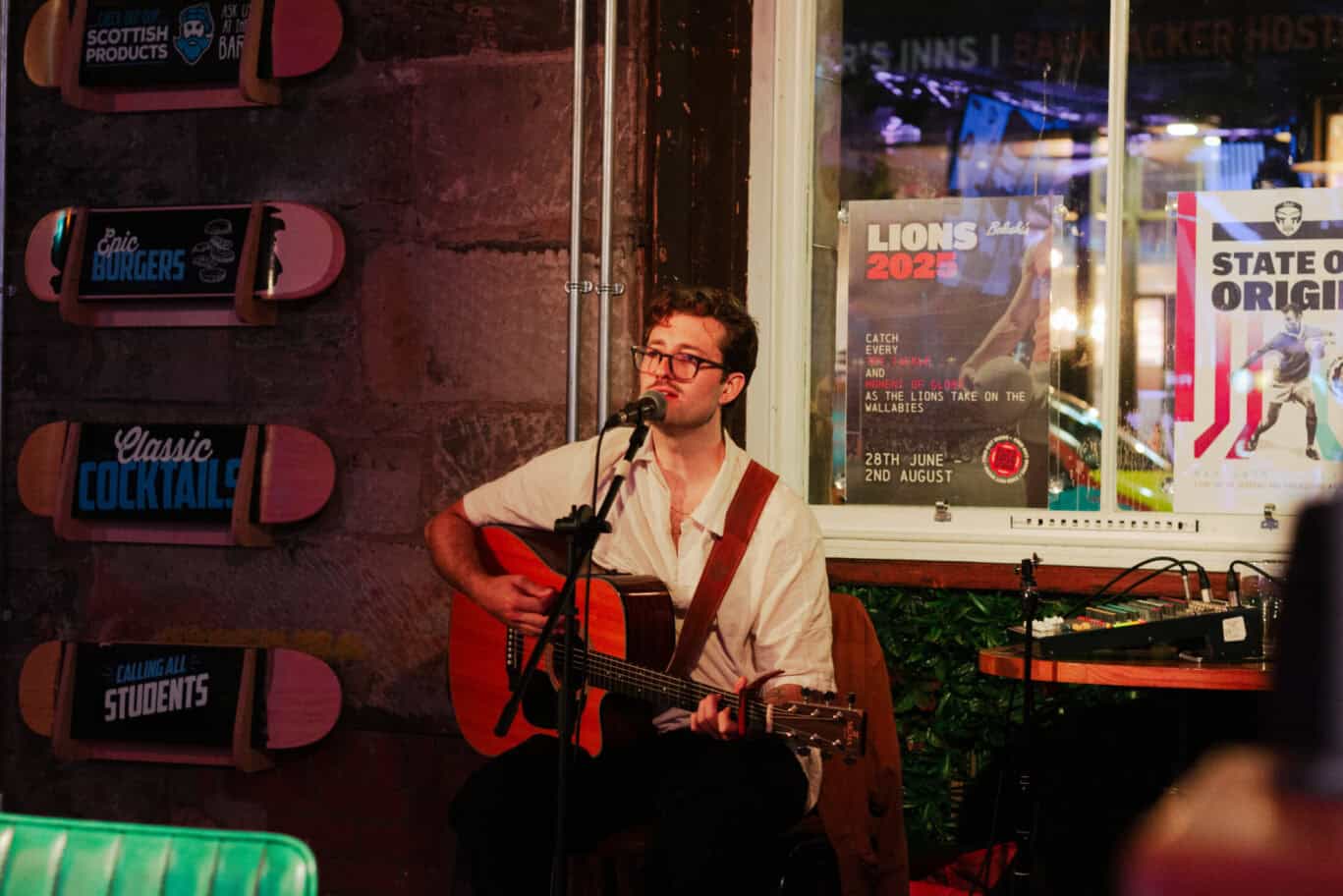 A musician playing guitar and singing into a microphone at a lively venue in Edinburgh.