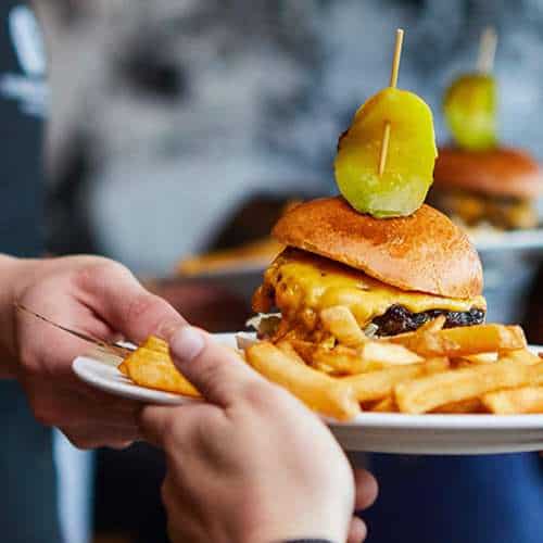 Cheeseburger with melted cheese, pickles, and fries served on a plate.
