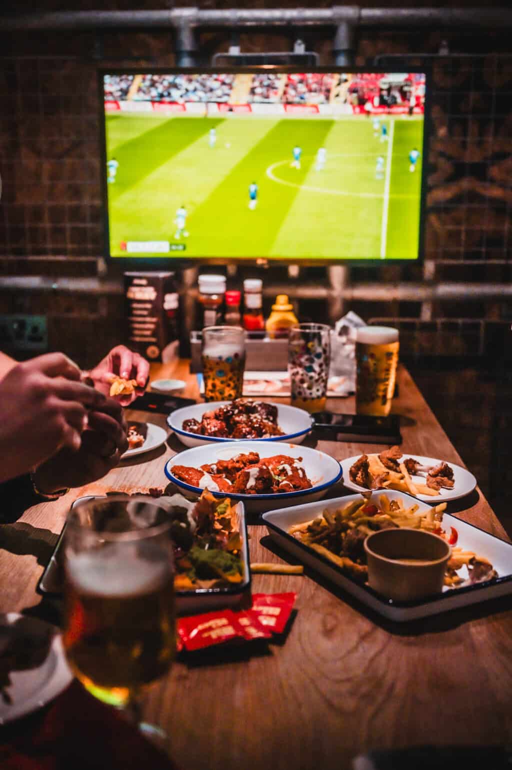 Indoor bar scene at Canal Hostel with football game on TV and food and drinks on the table.