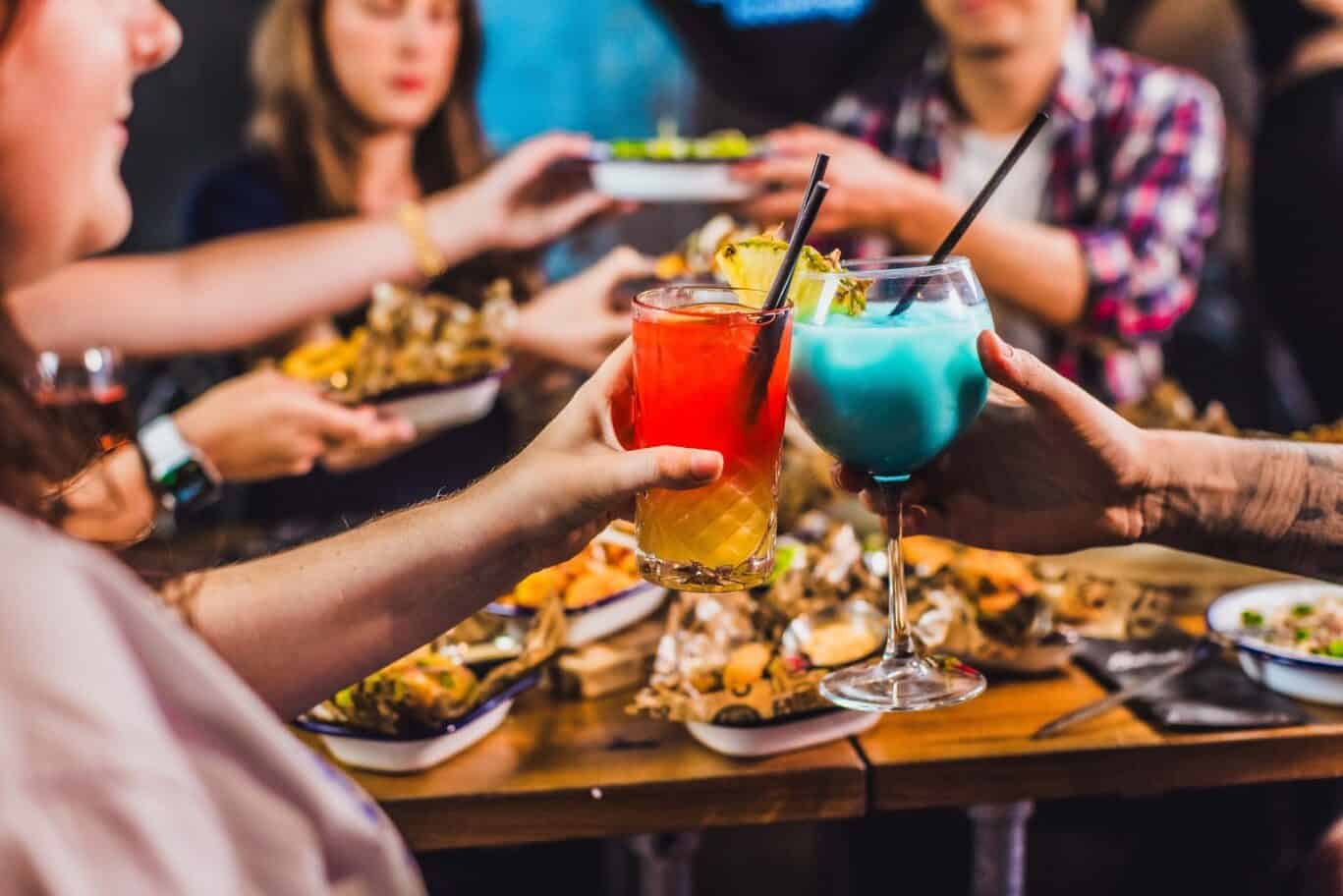 Group of friends enjoying colourful cocktails at a lively canal-side restaurant in Paris.