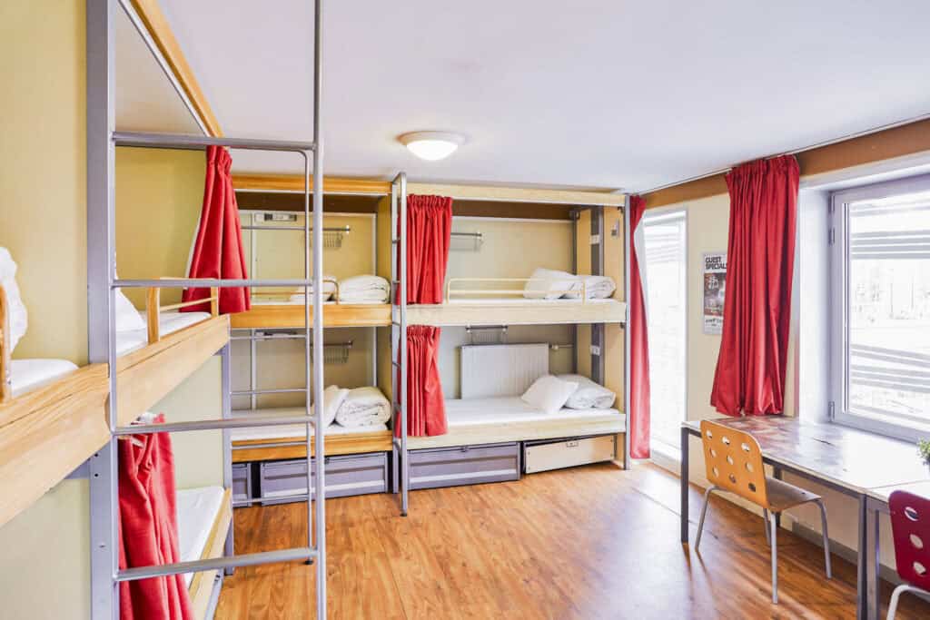 Modern hostel dorm with bunk beds and red curtains.