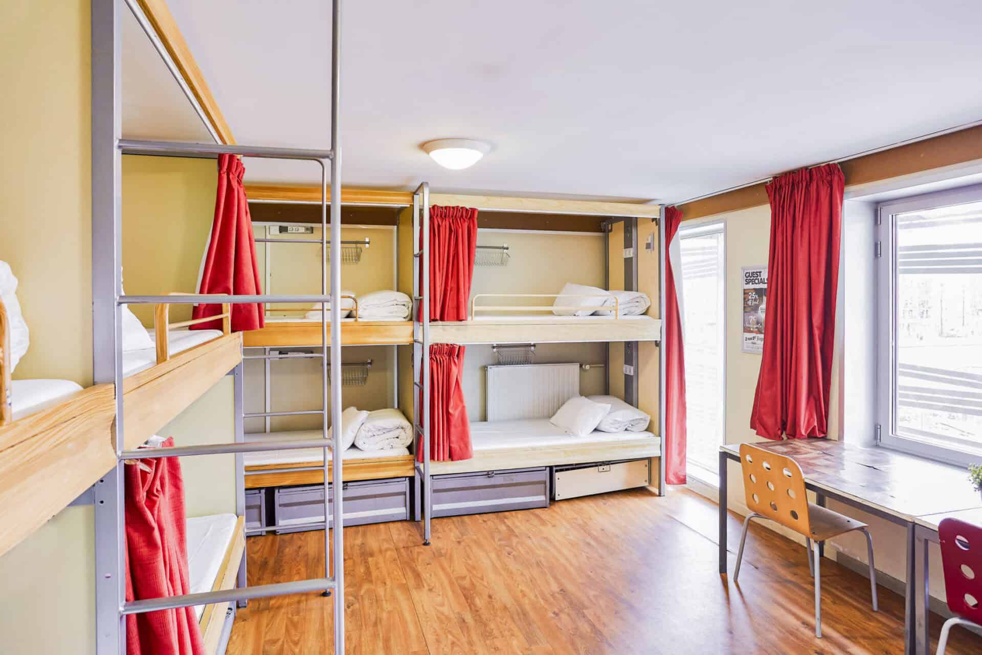 Modern hostel dorm with bunk beds and red curtains.