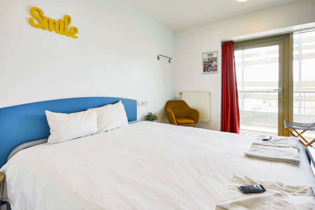 Bright hostel room at St Christopher’s Paris - Canal with large bed and balcony view.