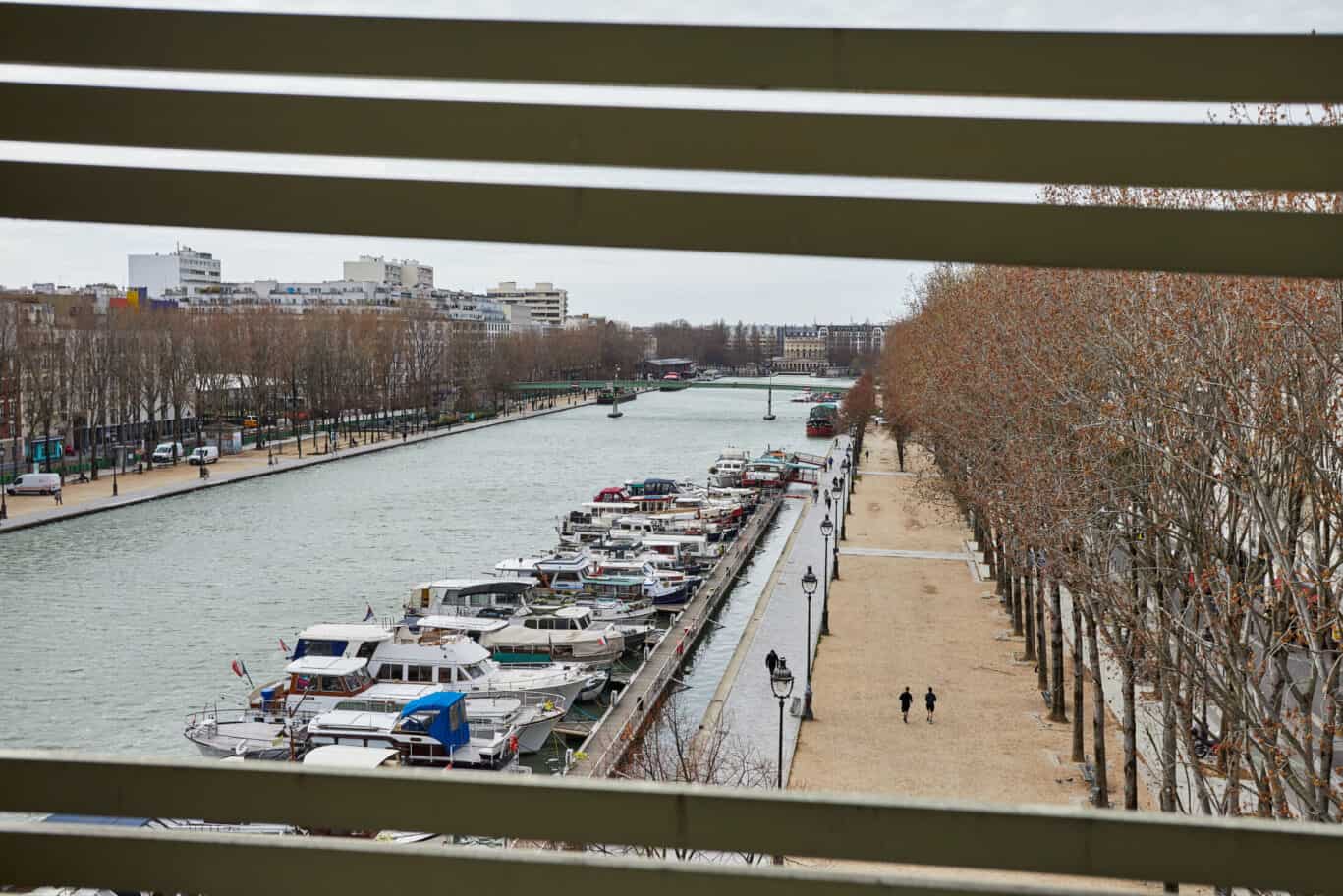 View of the canal with boats and trees in Paris, seen from a window.