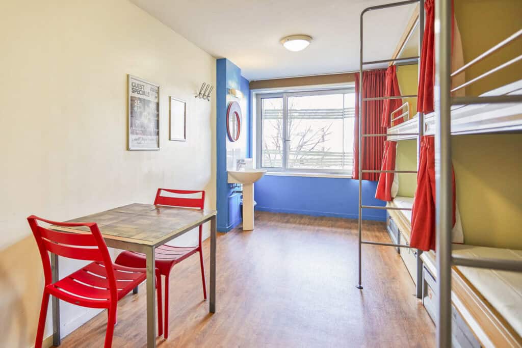 Bright hostel room with bunk beds and seating area.