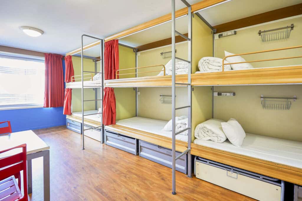 Hostel dorm room with bunk beds, colourful curtains, and wooden flooring at St Christopher’s Paris -.
