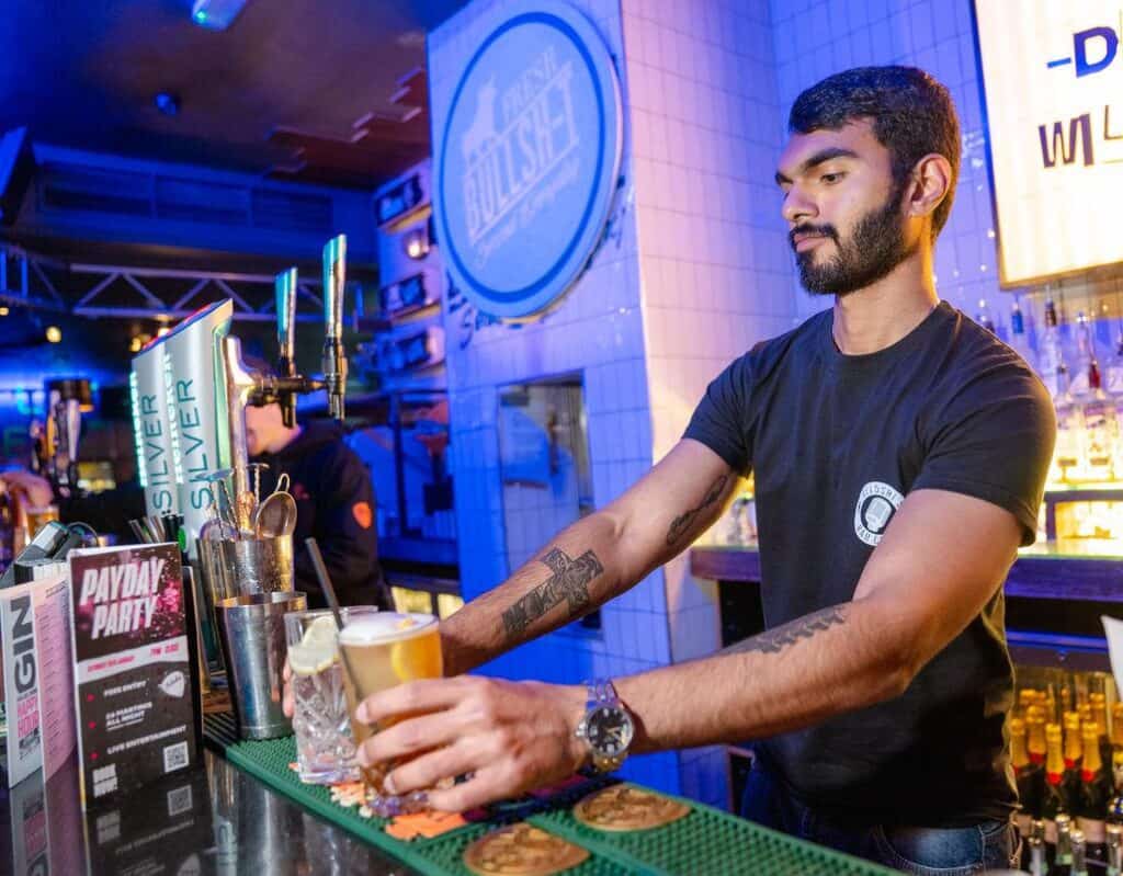 Young bartender preparing drinks at Shepherd's Bush Hostel bar in London.