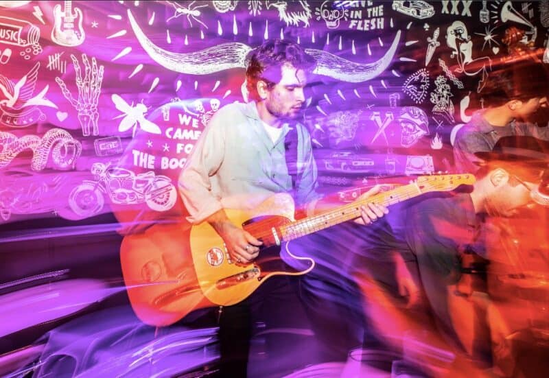 Young man playing electric guitar during live music event at Vienna hostel.