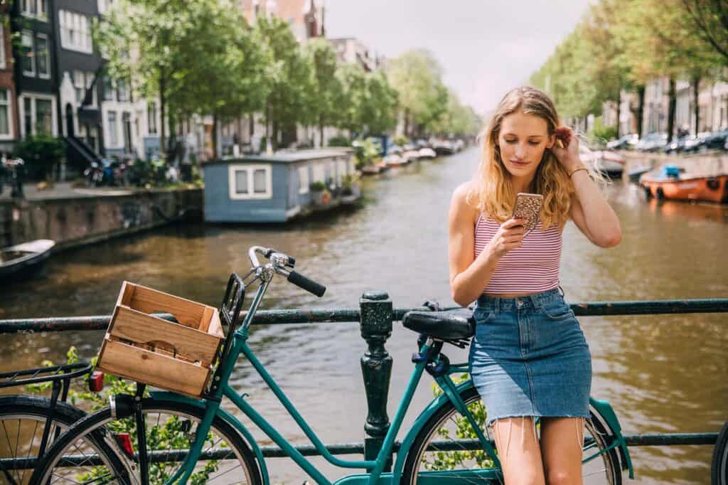Young woman using her phone beside a bicycle on a canal in Berlin's Mitte district.