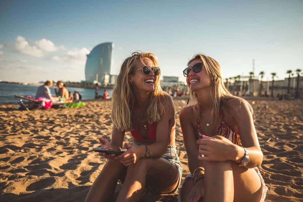 Two women relaxing on Berlin beach with city skyline in background.