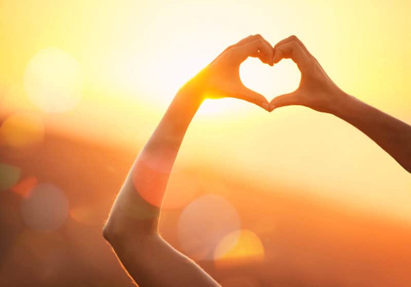 Hands forming a heart shape at sunset in Berlin, symbolising love and friendship.