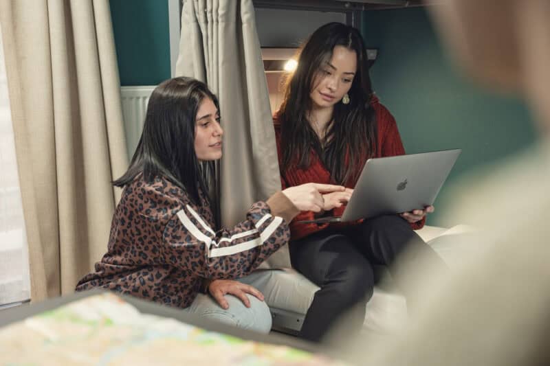 Two women engaging in a support group session, one with a laptop, in a comfortable indoor setting.