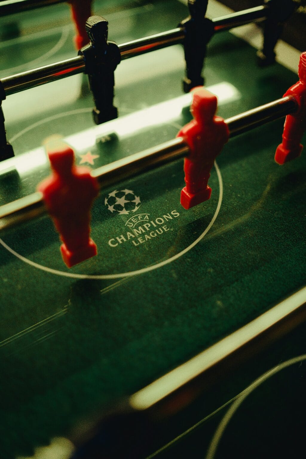 Foosball table with red and blue players, UEFA Champions League logo visible underneath, lively spor.