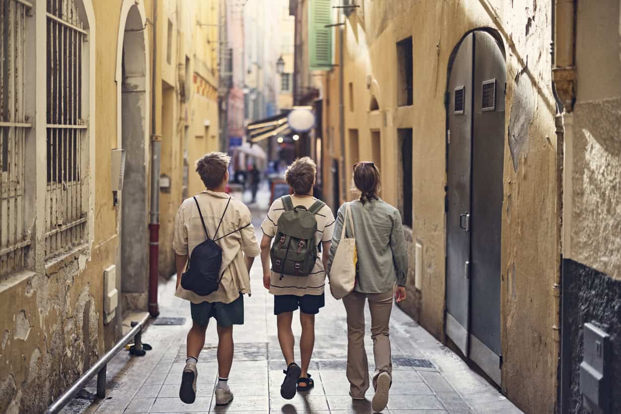 Three young friends walking through a narrow European street with colourful buildings.