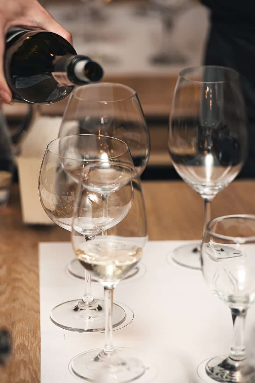 Pouring white wine into glasses at a dinner table.