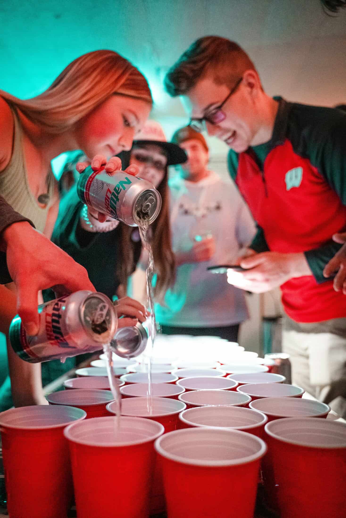People pouring drinks at a social event, with red cups and lively atmosphere.